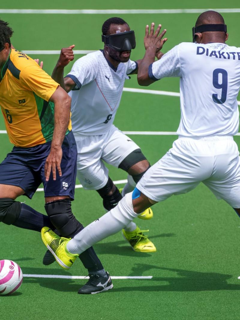 A Brazilian player breaks through a tackle from two French players in a blind football match at Tokyo 2020.